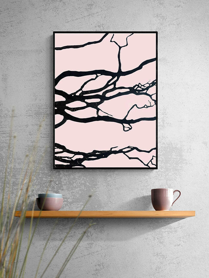 Abstract art print with black lines on a pink background in a black frame, displayed on a gray wall above a wooden shelf.