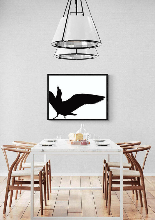 Dining room with a white table and chairs, a black and white art piece of a seagull in silhouette on the wall, and a pendant light.