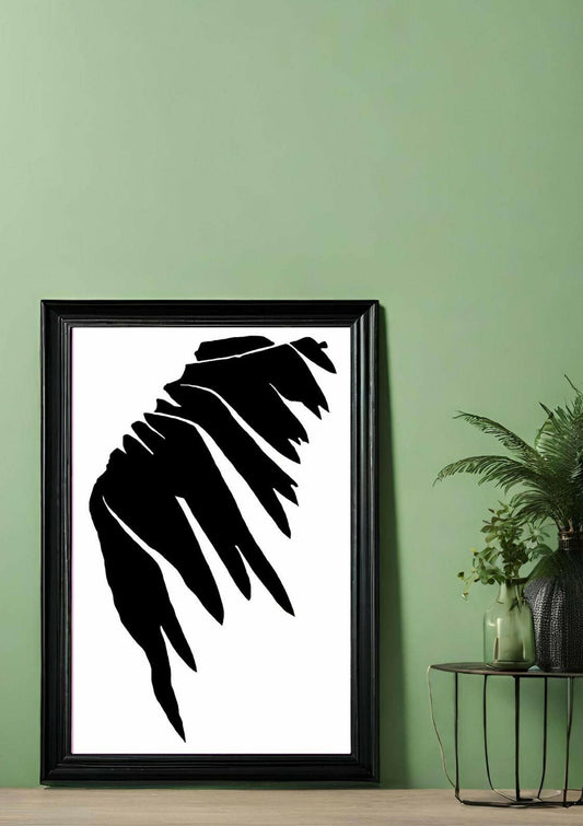 Printable wall art of an abstract nature-inspired shape in black, on a white background, framed in a black frame, leaning against a green wall.