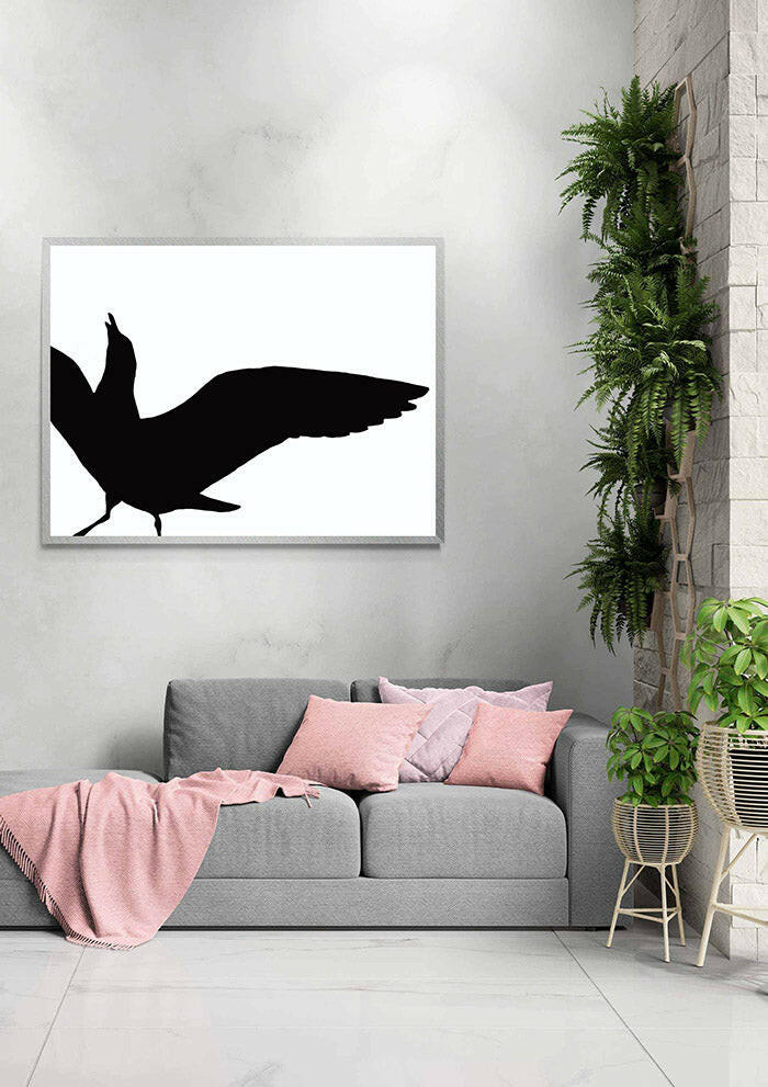 Framed artwork of a black seagull in silhouette on a white wall above a gray sofa with pink cushions.